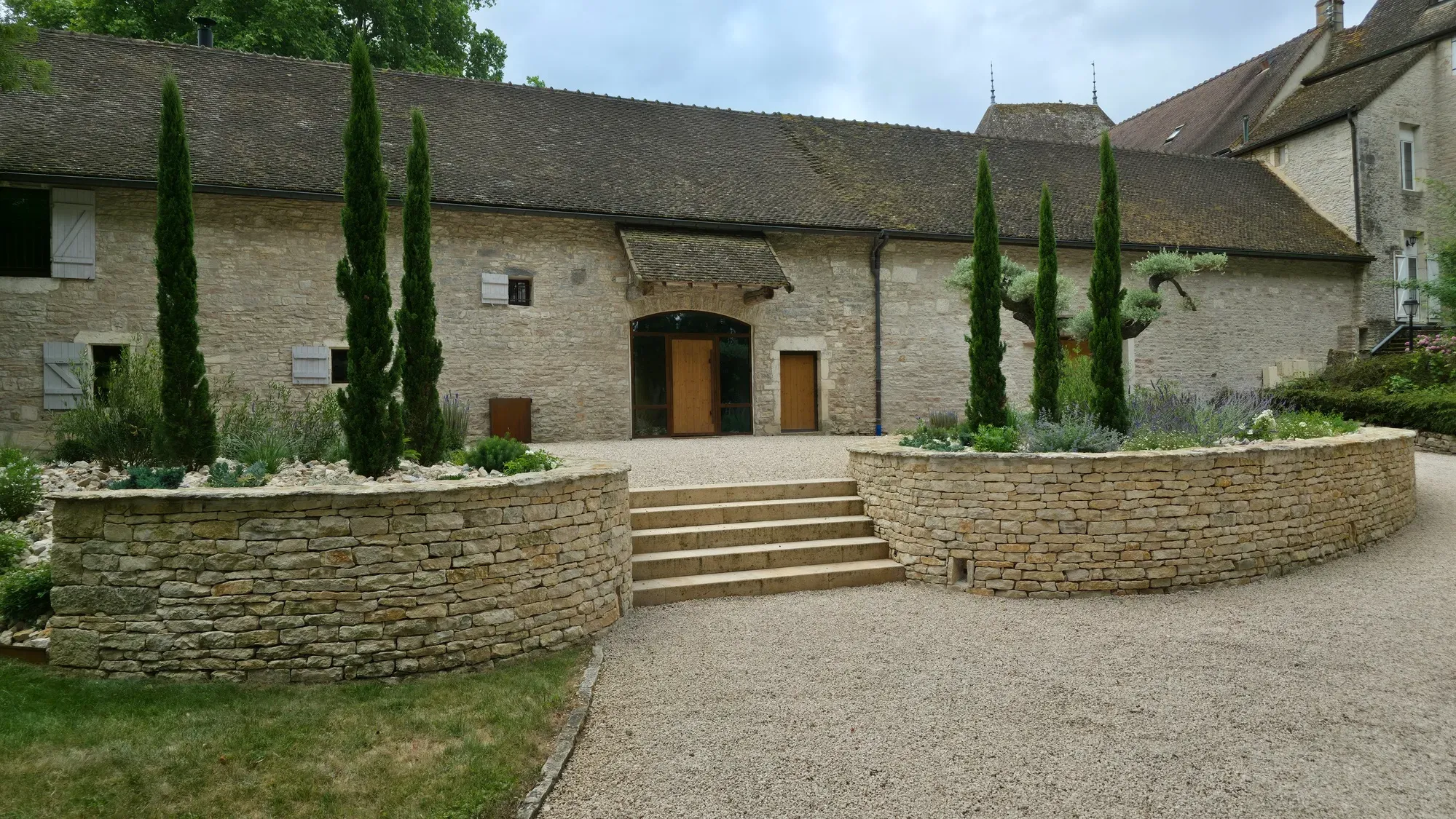 Massifs surélevés en pierre sèche, cyprès et escalier aménagés dans une cour en gravier – Hortiplan Paysagiste