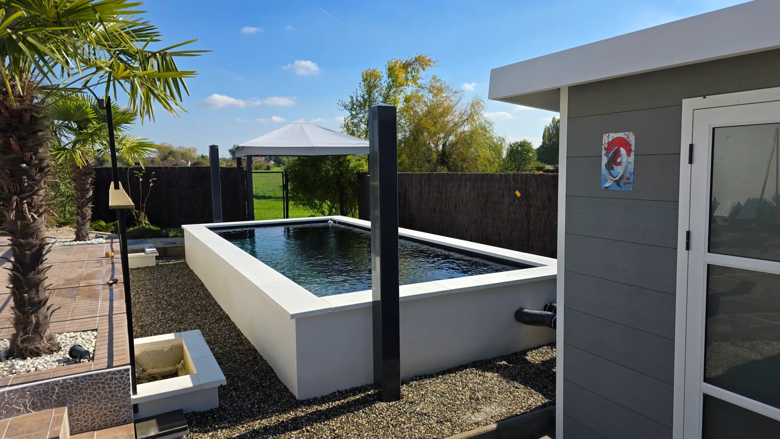 Mini-piscine hors-sol blanche intégrée à une terrasse contemporaine avec palmiers – Hortiplan Paysagiste