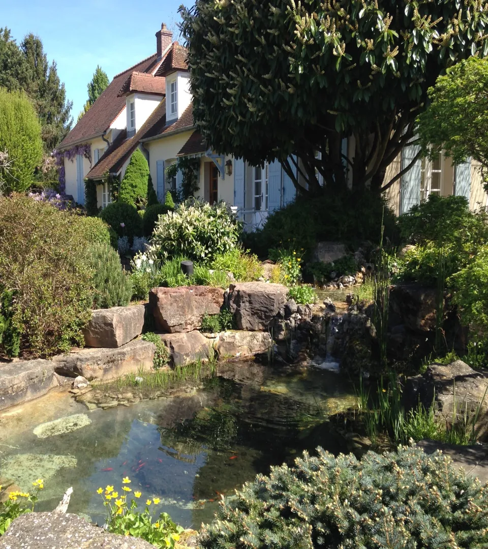 Bassin de jardin avec cascade en rocaille et massifs fleuris devant une maison, création de bassin Chagny 71150 – Hortiplan Paysagiste
